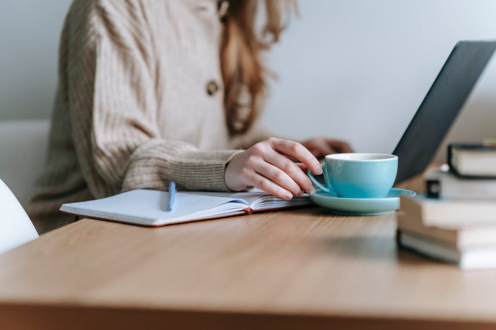 Crop anonymous female freelancing with netbook at table with mug of coffee on blurred background